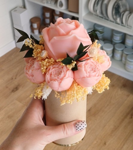 Pachnący flower box z wosku sojowego z brzoskwiniową różą, cielistymi suszkami i zielonymi listkami w beżowym pudełku welurowym.